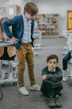 Two boys in a school library scene depicting a bullying incident, highlighting peer conflicts.